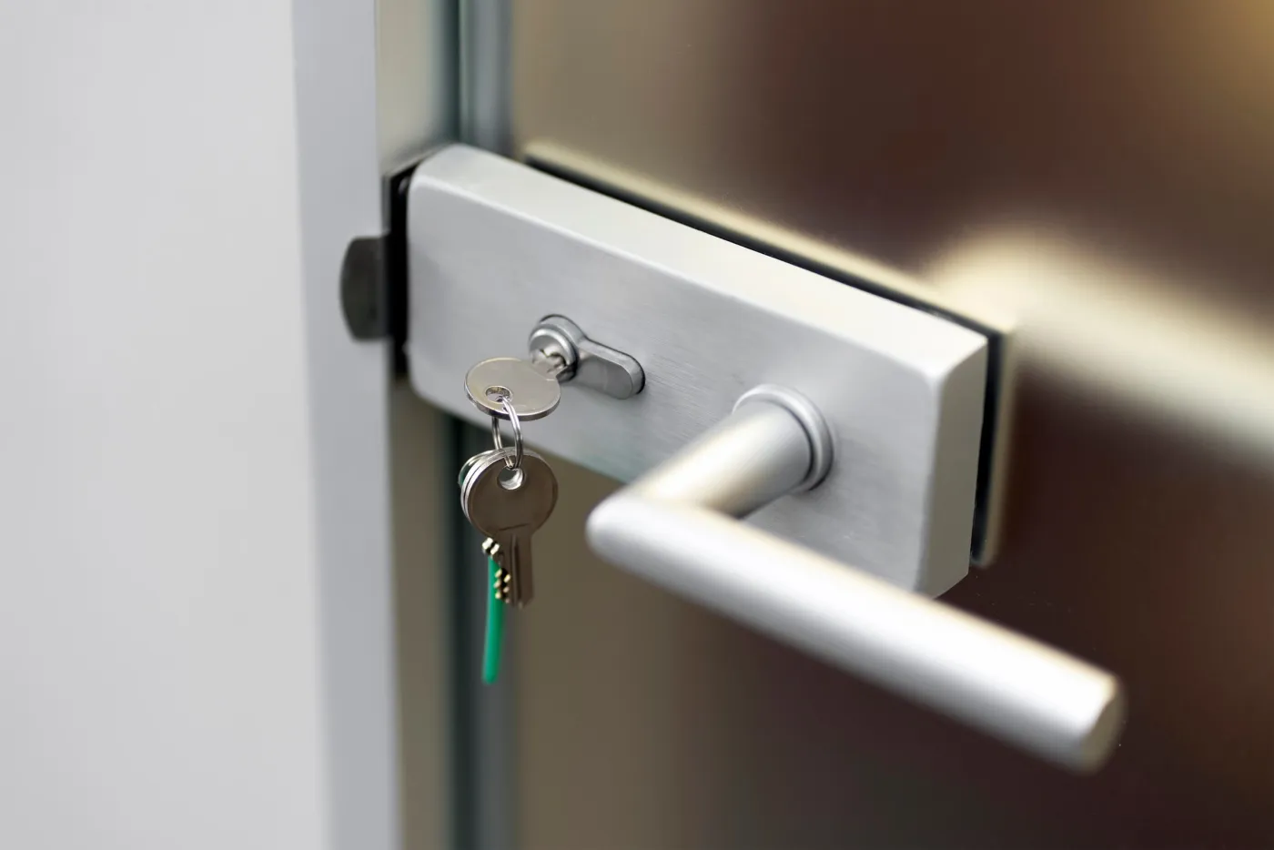 Gros plan d'une serrure en applique en acier brossé et de sa clé sur une porte vitrée d'un hall d'immeuble du quartier Champ-de-Mars